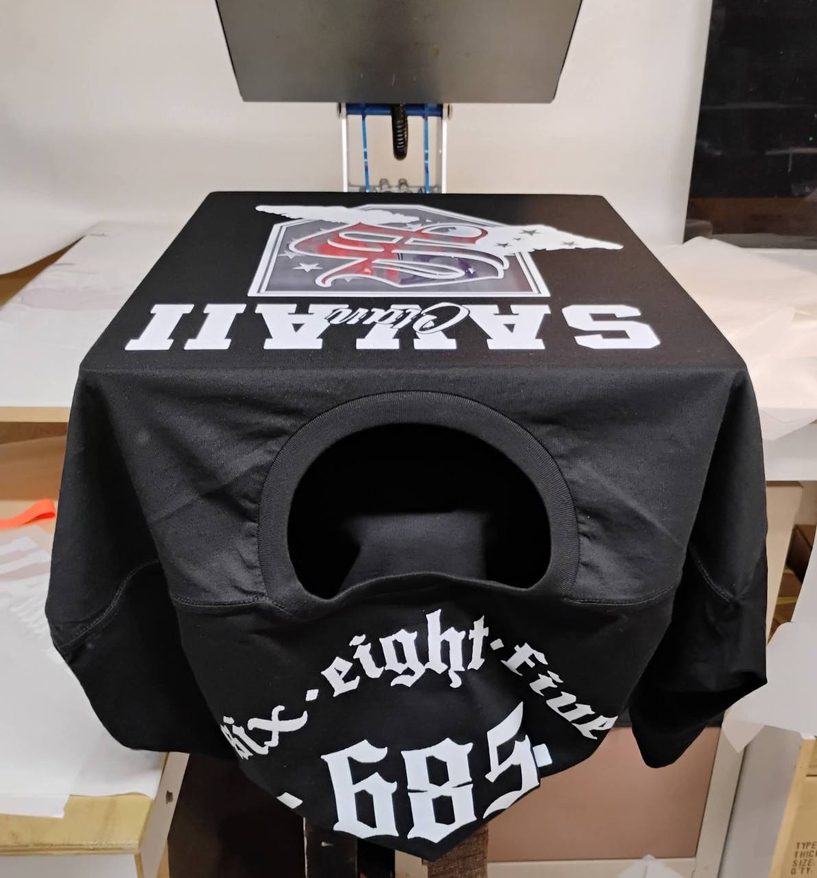 Black T-shirt on a heat press with red and white artwork and large white 685 lettering.