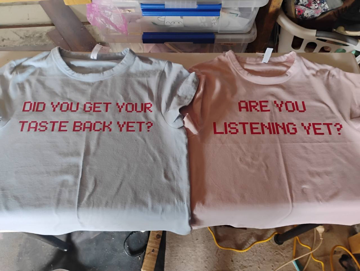 Grey and pale pink T-shirts with personalised red text: “Did you get your taste back yet?” and “Are you listening yet?”
