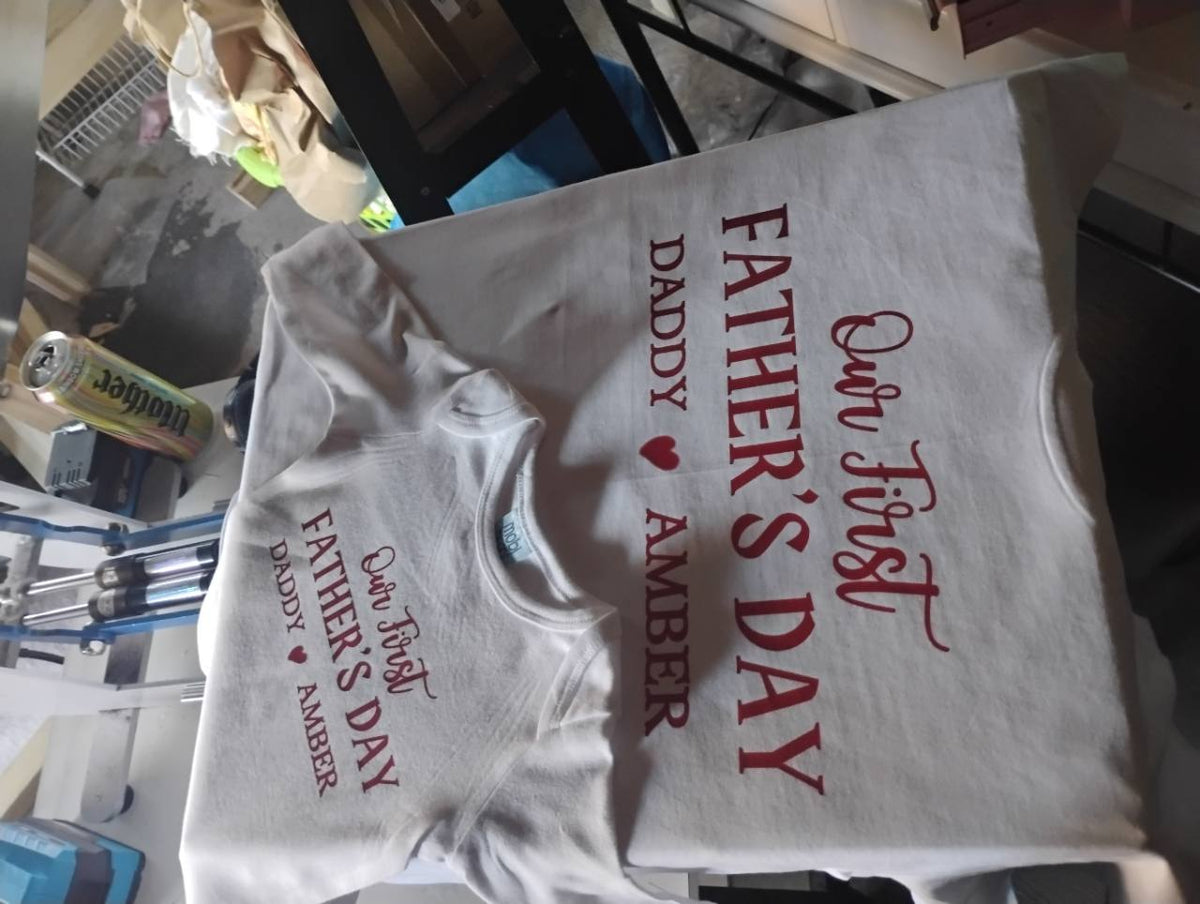 White adult T-shirt and baby bodysuit printed with red “Our First Father’s Day” and “Daddy ♥ Amber” lettering.