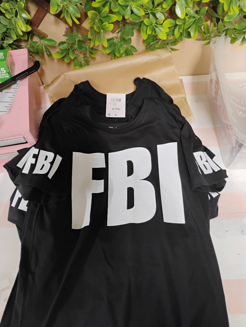 Stacked black T-shirts with large white FBI lettering on the fronts and sleeves.