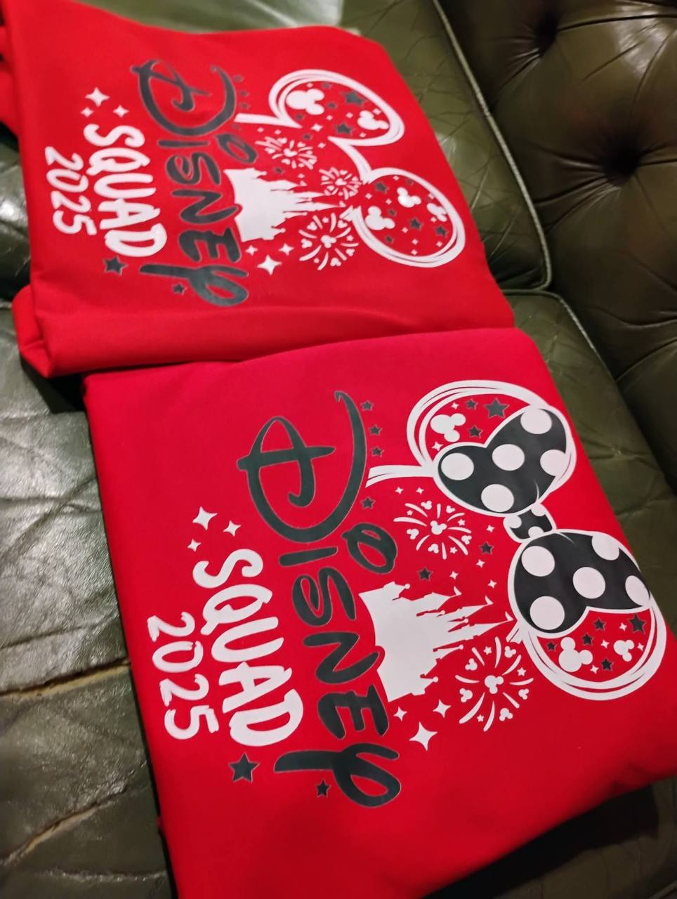 Two red shirts printed with Disney Squad 2025 lettering, castle silhouettes and mouse-ear designs.