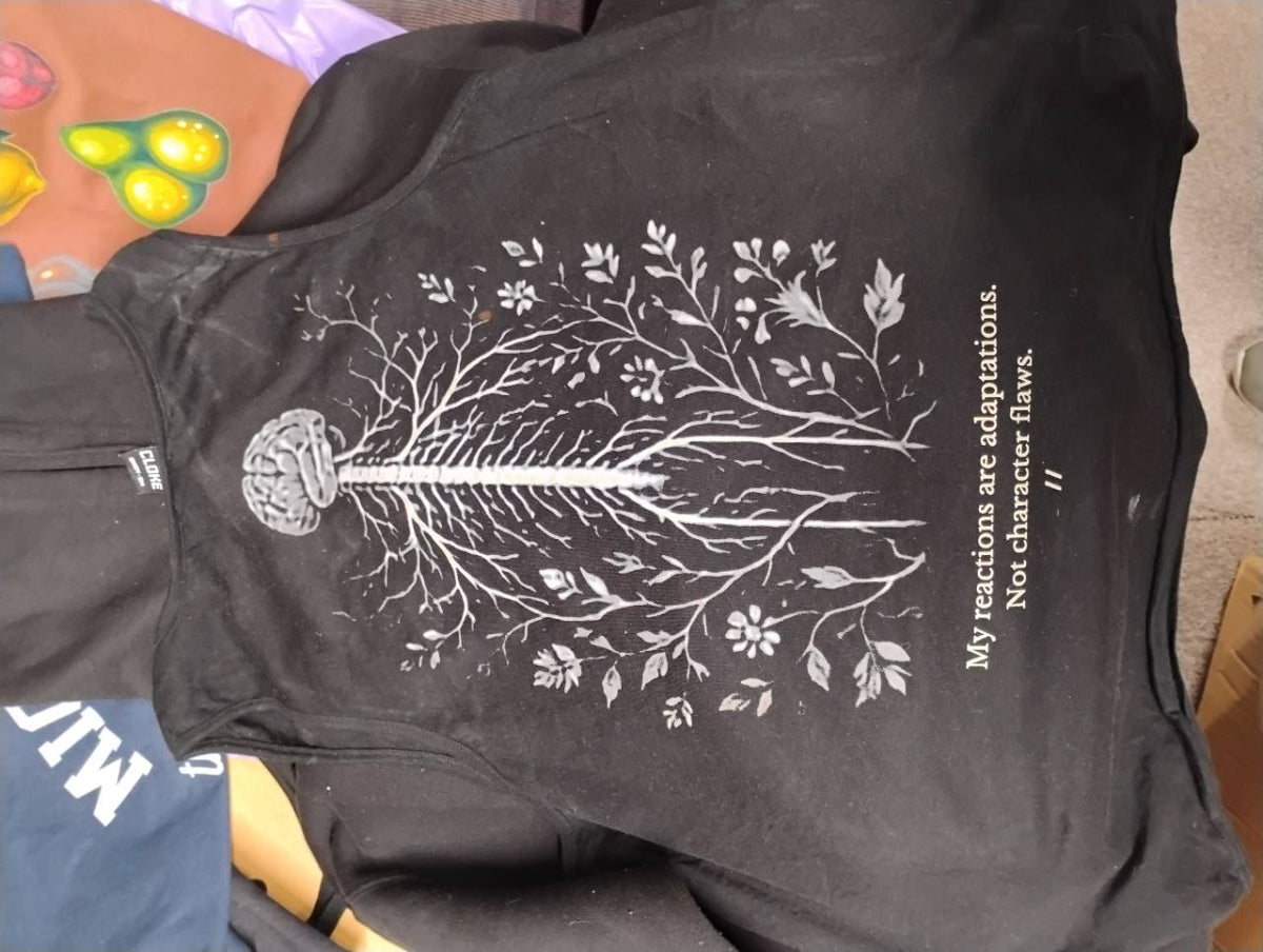 Black T-shirt with a white brain-and-branching design and the words “My reactions are adaptations. Not character flaws.”