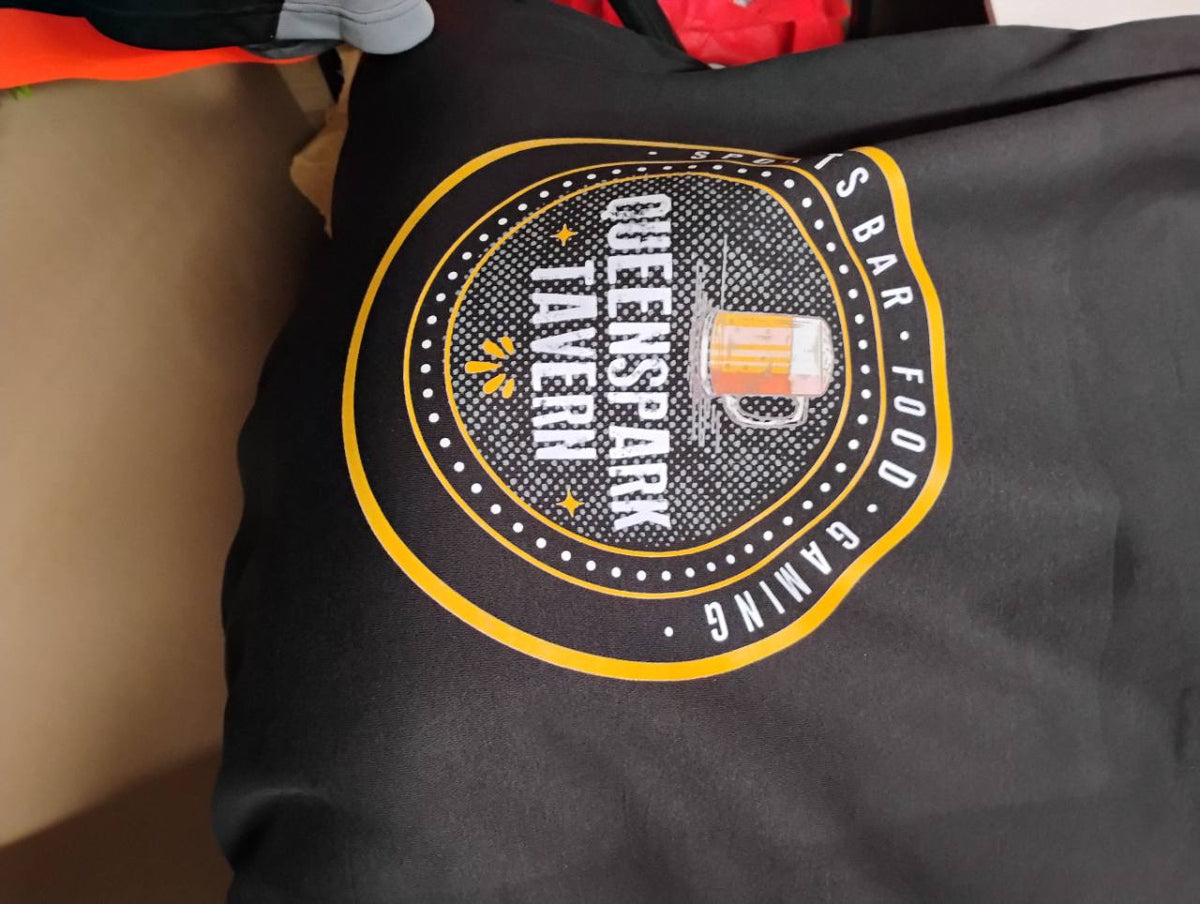 Large white-and-yellow Queenspark Tavern logo printed on black fabric, featuring a beer-mug illustration.