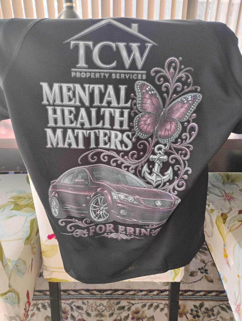 Black TCW shirt with “Mental Health Matters” and “For Erin” lettering, a pink butterfly, anchor and burgundy car.